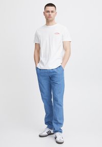 Camiseta blanca de algodón con estampado rojo en el pecho, combinada con pantalones azul claros y zapatillas en blanco y negro. Conjunto simple y casual.