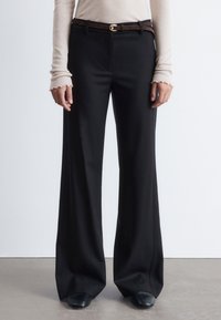 Black wide-leg trousers made of smooth fabric, featuring a front crease and a brown leather belt with a gold buckle.
