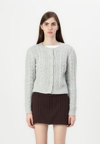 Light gray knitted cardigan featuring a cable design, round neckline, ribbed cuffs, and five button closures, paired with a dark skirt.