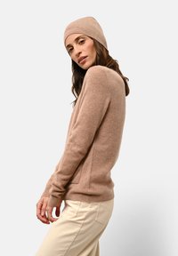Maglione lavorato a maglia beige con vestibilità rilassata, pannelli laterali e polsini a coste, abbinato a un berretto a coste coordinato, indossato con pantaloni color crema.