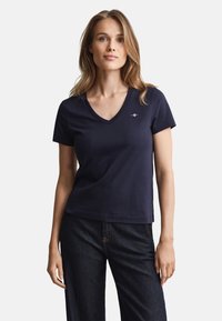 Tricou bleumarin cu decolteu în V, mâneci scurte, din bumbac, cu un logo mic pe piept. Asortat cu blugi din denim închis la culoare.