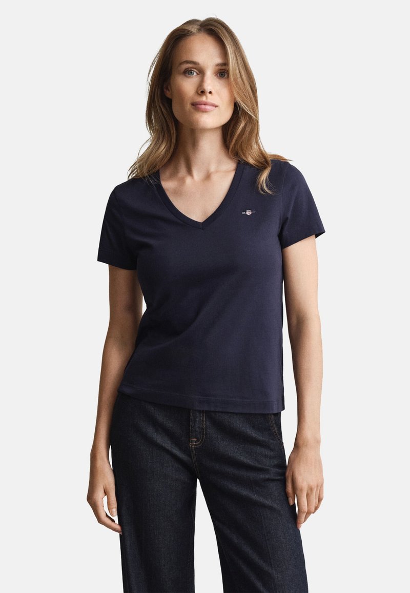 Temno modra majica z V-izrezom in kratkimi rokavi, iz bombaža, z majhnim logotipom na prsih. Kombinirana s temnimi denim jeans hlačami.