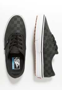 Czarne sneakersy Vans z subtelnym wzorem w szachownicę, białe gumowe podeszwy, czarne sznurówki i brązowy bieżnik pokazane z widoków z góry i z boku.
