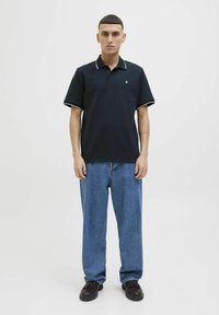 Tumes polo särk kontrastse valge krae ja mansettidega, tekstureeritud kangas, koos helesiniste lõtvade teksade ja tumedate kingadega. Minimalistlik disain.