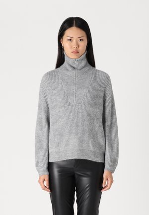 Pull à col roulé gris, côtelé, avec une fermeture éclair à mi-hauteur et une coupe décontractée. Matière en maille texturée. Assorti à un pantalon en cuir noir.