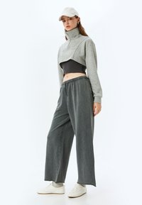 Grijze cropped sweatshirt met een hoge kraag, gecombineerd met losse grijze sweatpants en witte sneakers. Accentdetails omvatten een zwarte onderlaag.