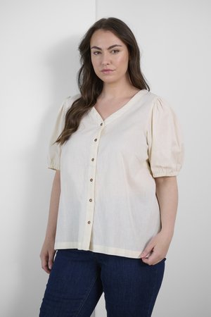 Crèmekleurig shirt met korte pofmouwen, v-hals en zes bruine knopen die langs de voorkant lopen. Zachte, lichte stof.