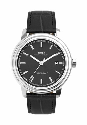 Timex Waterbury automatic watch with a black textured leather strap, silver casing, and black dial featuring silver hour markers and a date display.