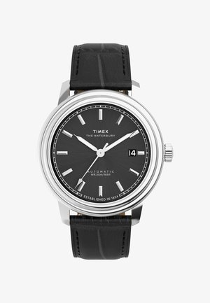 Timex Waterbury automatisk ur med et sort tekstureret læderrem, sølv hus og sort urskive med sølv time markører og en datovisning.
