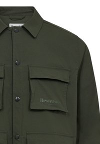 Olivově zelená košile s bundovým střihem vyrobená z látky s hladkým povrchem, s předním zapínáním na knoflíky, dvěma náprsními kapsami a detailem s logem.