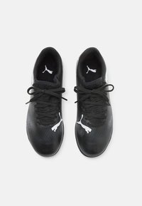 Zapatos deportivos negros con una superficie texturizada, acentos blancos y un sistema de cierre central con cordones. Presenta el logo de la marca en el lateral y en la lengüeta.