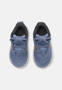 Baskets de sport de couleur bleu clair avec une tige en tissu texturé, un renfort au niveau des orteils, un col en mesh gris foncé et des accents orange sur les côtés.