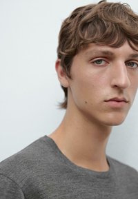 Gray, short-sleeve t-shirt with a soft texture. Close-up of a person's face with light brown hair and neutral-toned skin, eyes visible.