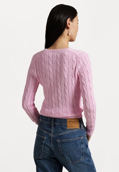 Light pink cable-knit sweater with a fitted silhouette, long sleeves, and round neckline, paired with dark blue denim jeans and a leather tag.