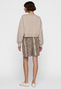 Sudadera corta beige con hombros caídos combinada con una falda de estampado de serpiente marrón, que presenta una textura suave y un patrón sutil.