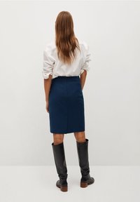 Jupe crayon bleu marine avec une taille mi-haute, des poches latérales et une fente à l'arrière. Associée à une chemise blanche surdimensionnée et des bottes noires jusqu'aux genoux.