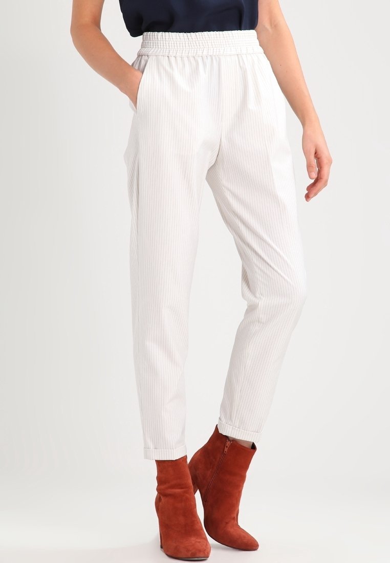 Pantalon à rayures blanches avec une ceinture élastique, doté de poches latérales et de jambes fuselées, associé à des bottines rouges en daim.
