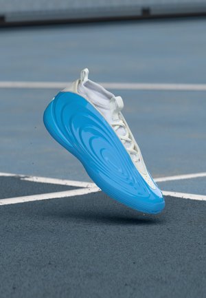 Letvægts atletisk sko med en struktureret hvid overdel og en blank blå sål med bølgemønstre. Designet fremhæver komfort og stil.