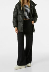 Černá péřová bunda s lesklým povrchem, zkrácený pruhovaný top a široké černé cargo kalhoty. Celý outfit doplňují robustní bílé tenisky.