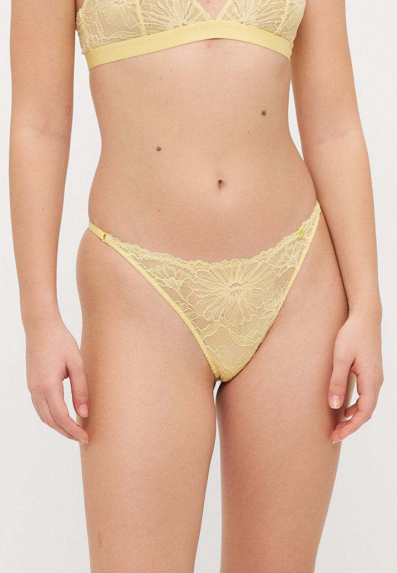 Gul blonder bralette med blomster mønster, med en glatt gul bånd. Matchende blondetanga med minimal dekning og justerbare stropper.