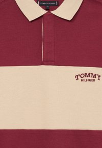 Burgunder- og beige-stribet polo shirt lavet af tekstureret stof, med krave og broderet "TOMMY HILFIGER" logo på brystet.