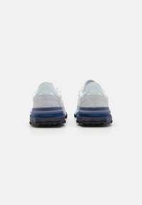 Scarpe da corsa bianche con accenti blu, pannelli grigi testurizzati e una suola in gomma nera con lugs di trazione. Vista posteriore della calzatura.