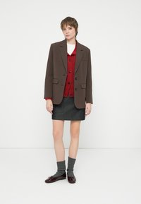 Sacou brun croițat peste un cardigan roșu, asociat cu o fustă gri. Purta șosete până la genunchi gri și pantofi burgundy. Design simplu și curat.