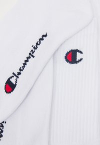 Weiße Baumwollsocken mit schwarzem "Champion"-Textlogo und einem runden roten und schwarzen Emblem. Gerippte Textur auf dem Stoff.