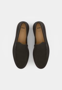 Des chaussures en cuir marron à enfiler, avec un bout rond, des coutures contrastées et un logo embossé sur le dessus. Texture lisse.