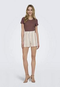 Shorts with vertical stripes in cream, beige, and rust, paired with a fitted mauve ribbed top. Model stands in nude heels on a light background.