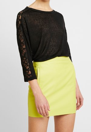 Czarna półprzezroczysta bluzka z kwiatowymi koronkowymi rękawami w połączeniu z jasnokropkową żółtą mini spódnicą z wysokim stanem.