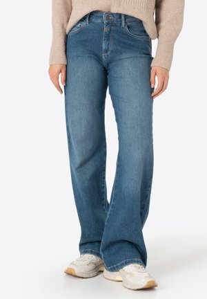 Hellblaue Jeans aus Denim mit hoher Taille, weiter Beinform und markanten Fronttaschen. Getragen mit cremfarbenen Sneakers und einem beigenPullover.