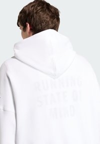 Λευκό φούτερ με μεγάλη κουκούλα, με ξεθωριασμένο κείμενο στην πλάτη που αναγράφει «RUNNING STATE OF MIND». Μαλακή υφή υφάσματος.