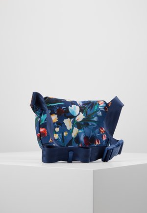 Marineblå crossbody taske i stof med flerfarvet blomsterprint og justerbar rem med plastikspænde på hvid overflade.