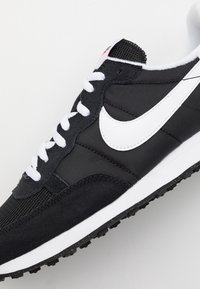 Baskets Nike noir et blanc avec lacets blancs, empeigne en mesh et suède, et logo Nike Swoosh blanc sur le côté.