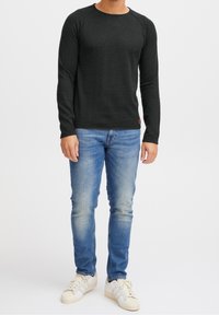 Chemise noire à manches longues en tissu doux, col rond et manches raglan, associée à un jean bleu clair et des baskets blanches.