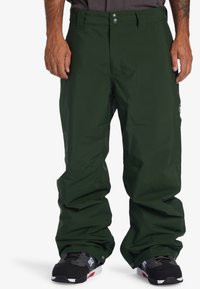 Green waterproof snow pants with a relaxed fit, featuring a button closure, side pockets, and a logo patch on the left thigh.