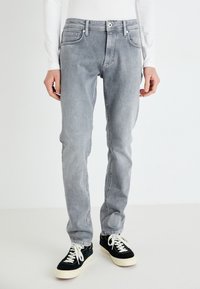 Vaqueros de mezclilla gris con un corte recto, diseño de cinco bolsillos y una textura ligeramente desgastada. Combinados con zapatillas negras y cordones blancos.