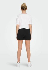 White short-sleeve t-shirt paired with black shorts. The shorts are streamlined, with a smooth texture, ankle-length, and worn with white sneakers.