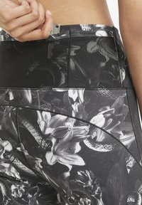 Legginsy z wysokim stanem w kwiatowy wzór w kolorze czarnym i szarym, charakteryzujące się gładką teksturą, kontrastowymi szwami oraz ukrytą kieszenią z tyłu.