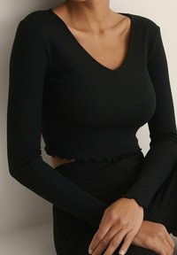 Schwarzes geripptes Langarm-Crop-Top mit V-Ausschnitt und Rüschensaum. Glatte Textur mit taillierter Passform; kombiniert mit passenden schwarzen Unterteilen.