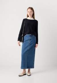 Temno modra pletena jakna z belim ovratnikom, kombinirana z dolgo modro jeans krilo. Manekenka nosi svetle balerinke in nosi črno torbico.