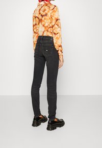 Svarta denim skinny jeans med bakfickor, kombinerat med en långärmad skjorta i orange tie-dye och svarta plattformsskor med texturerade sålar.
