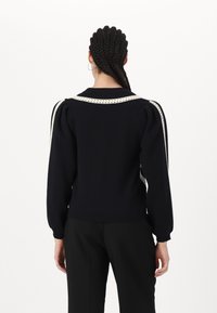 Granatowy sweter z dzianiny o bufiastych rękawach, z białym plecionym detalem wzdłuż ramion. Gładka tekstura i dopasowany krój.