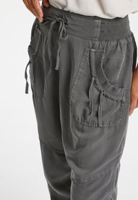 Grå bomullsjoggingbyxor med elastisk midja, dragsko och flera framfickor. Texturerad tyg med synlig sömnad.