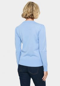 Maglione azzurro chiaro lavorato a maglia con scollatura tonda e orlo a coste aderente. Presenta spalle a palloncino e maniche lunghe e aderenti.