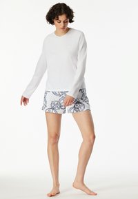 Vit långärmad topp i kombination med ljusfärgade shorts med ett blått blommönster. Shortsen har en elastisk midja för bekvämlighet.