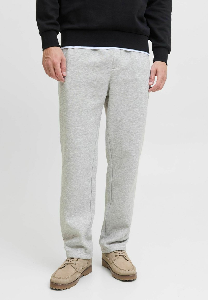 Lichtgrijze sweatpants gemaakt van zachte stof, met een relaxed fit en zijnaad, gedragen met een zwart sweatshirt en beige schoenen.