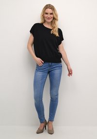 Černé triko s krátkým rukávem v uvolněném střihu, kombinované s světle modrými skinny džíny a taupe lodičkami. Hladká textura, jednoduchý design.
