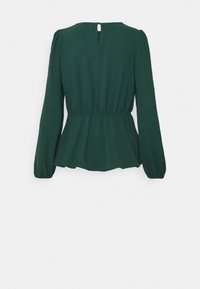 Blusa peplum verde scuro con maniche lunghe, dettagli arricciati in vita e apertura a chiave sulla schiena. Tessuto morbido.